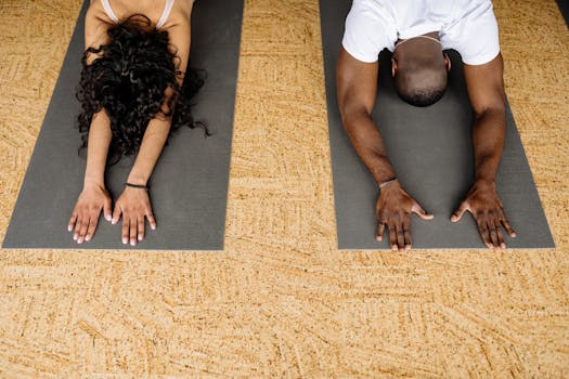 A man and woman performing yoga exercises on mats in a studio environment.