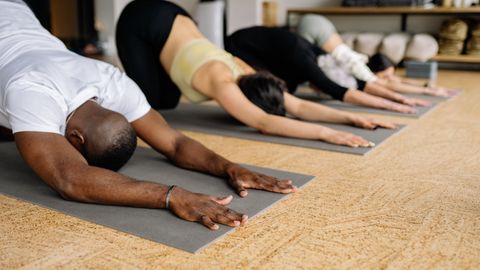 People practicing yoga indoors on mats, focusing on child pose.