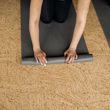 Hands rolling up a yoga mat on a cork floor, ready for indoor exercise.