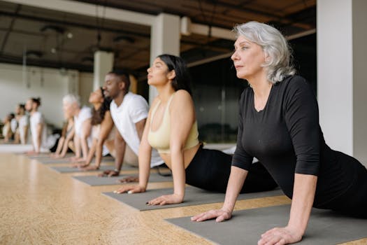 A diverse group of adults in a yoga class, practicing stretching on mats indoors.