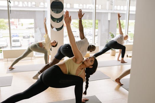 A diverse group of adults practicing yoga poses in a bright, modern studio with large windows.