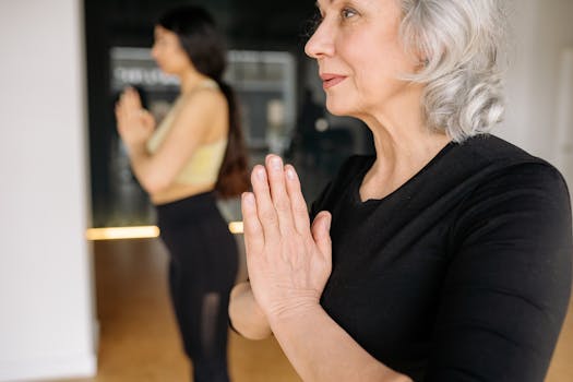 Elderly woman performs yoga namaste pose, promoting wellness and mindfulness indoors.