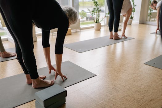 Participants bending forward in a sunlit yoga studio practicing wellness and flexibility.