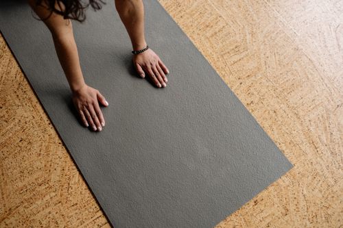 Free Close-up of hands on a grey yoga mat on a wooden floor, from above. Stock Photo