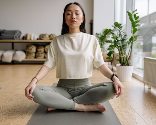 Free Woman sitting cross-legged on a yoga mat indoors, eyes closed, conveying peace and relaxation. Stock Photo