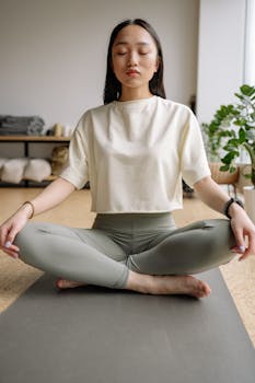 Tranquil scene of a woman meditating on a yoga mat indoors, promoting relaxation and wellness.