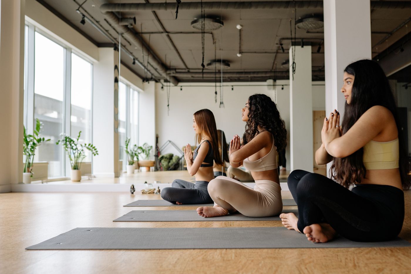Tres mujeres sentadas meditando con las manos en el pecho en clase de yoga