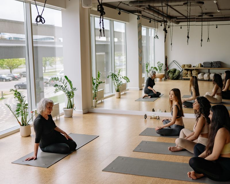 A yoga instructor guiding a seated group class in a sunlit studio