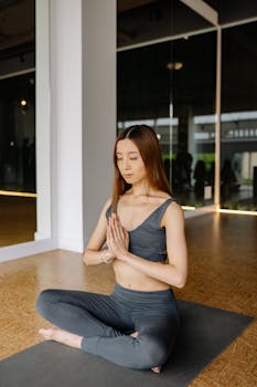 Focused woman in activewear practicing meditation indoors on a yoga mat.