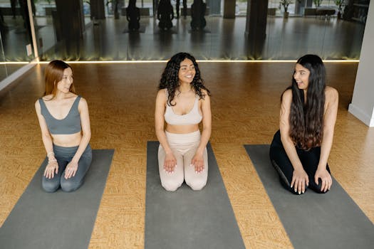 Three women in sportswear kneeling on yoga mats during a class.