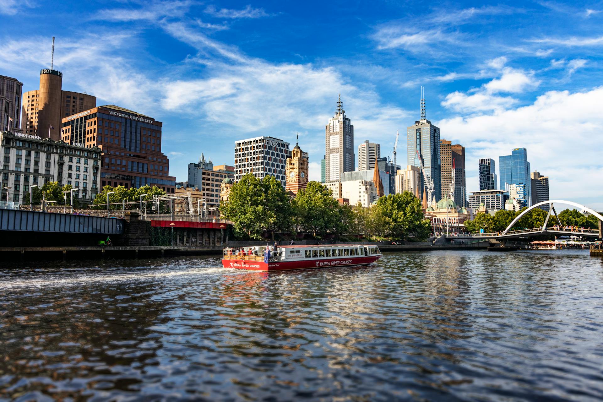 A scenic view of Melbourne's modern skyline along the Yarra River featuring a vibrant cruise boat.