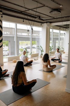 A diverse group practicing yoga in a sunlit studio with large windows.
