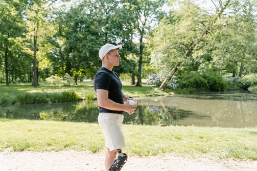 Man with a prosthetic leg enjoying a sunny day in the park, holding a cup.
