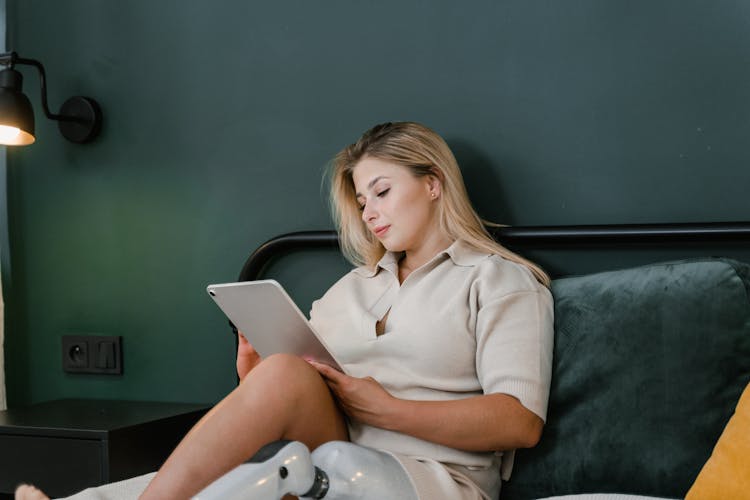 Woman Using A Tablet Sitting On A Bed