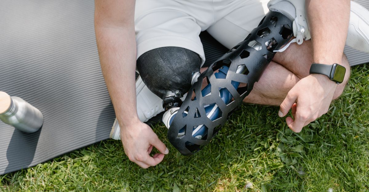 Close-up of a person with a prosthetic leg sitting on grass with exercise mat, embracing a healthy lifestyle.