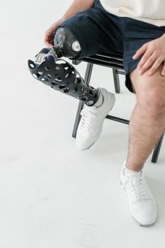 Detailed view of a person with a prosthetic leg sitting on a metal chair indoors.
