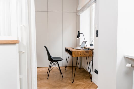 Elegant minimalist home office corner with wooden desk, laptop, and black chair for a serene workspace setting.