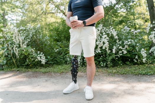 A man with a prosthetic leg stands outdoors holding a cup, surrounded by lush greenery.