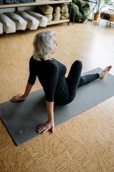 Elderly woman in black exercising on yoga mat indoors, promoting wellness and a healthy lifestyle.
