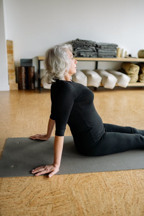 Elderly Woman in Black Clothing Sitting on Yoga Mat