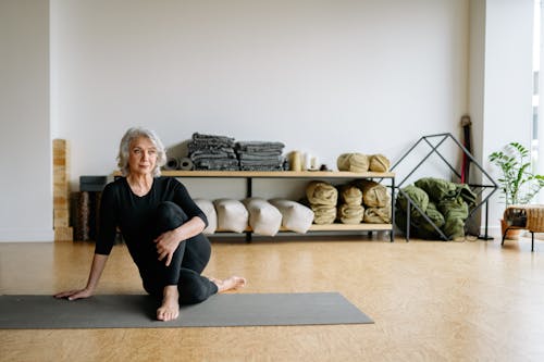 Elderly woman performing yoga exercise indoors on a mat, in a calm and serene setting.