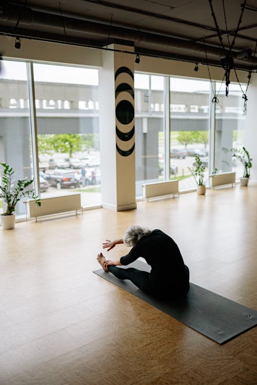 Woman Sitting on Yoga Mat While Doing Stretching