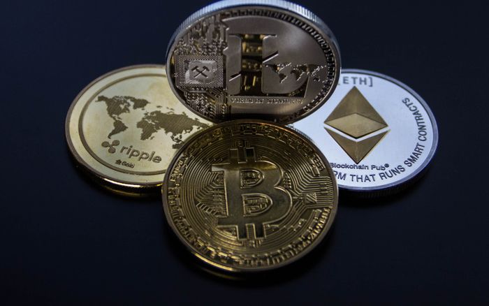 Physical cryptocurrency coins, including a Ripple XRP coin, on a dark surface.