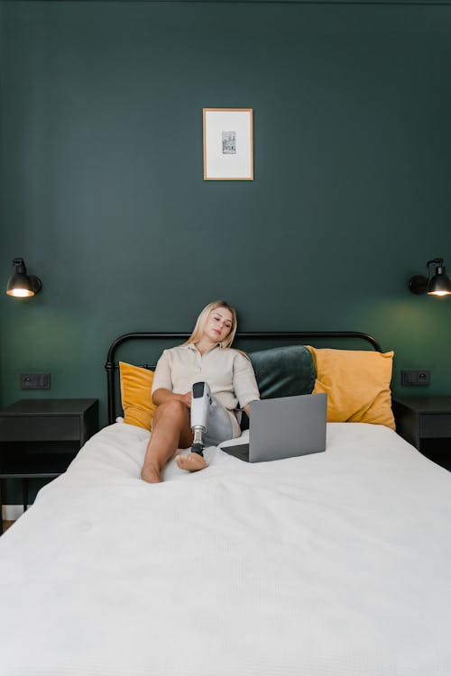 Woman in White Shirt Sitting on the Bed while Using Laptop