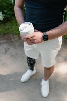 Close-up of a man holding a coffee cup, showcasing his prosthetic leg and smartwatch.