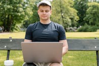 Close-Up Shot of a Man Using a Laptop while Sitting on a Wooden Bench