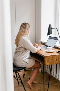 A woman sitting at a wooden desk using a laptop in a home office setting.