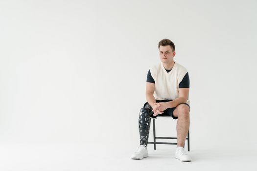 Portrait of a young man with a prosthetic leg sitting in a minimalist studio setting.