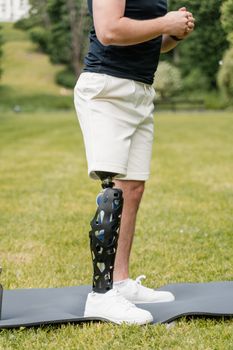 An individual with a prosthetic leg exercising on a mat in a sunny park setting.