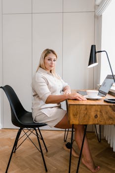 Woman working at home office desk with laptop, lamp, and coffee cup.