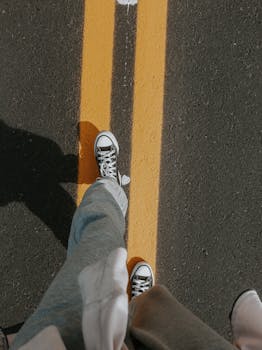 Overhead shot of casual walk on road with sneakers and yellow line, showcasing perspective.