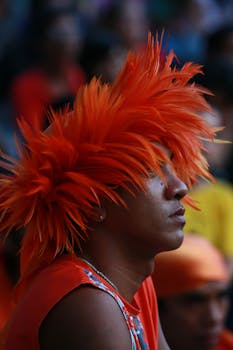 Man with bright orange wig at an outdoor festival, showing cultural pride.