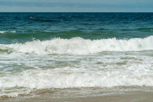 Lively ocean waves crash onto the sandy beach, showcasing the beauty of nature and the sea's vibrant energy.