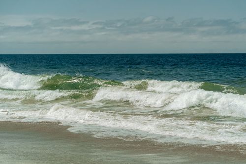 Free Dynamic ocean waves roll toward a sandy beach under a bright sky, capturing the essence of seaside nature. Stock Photo