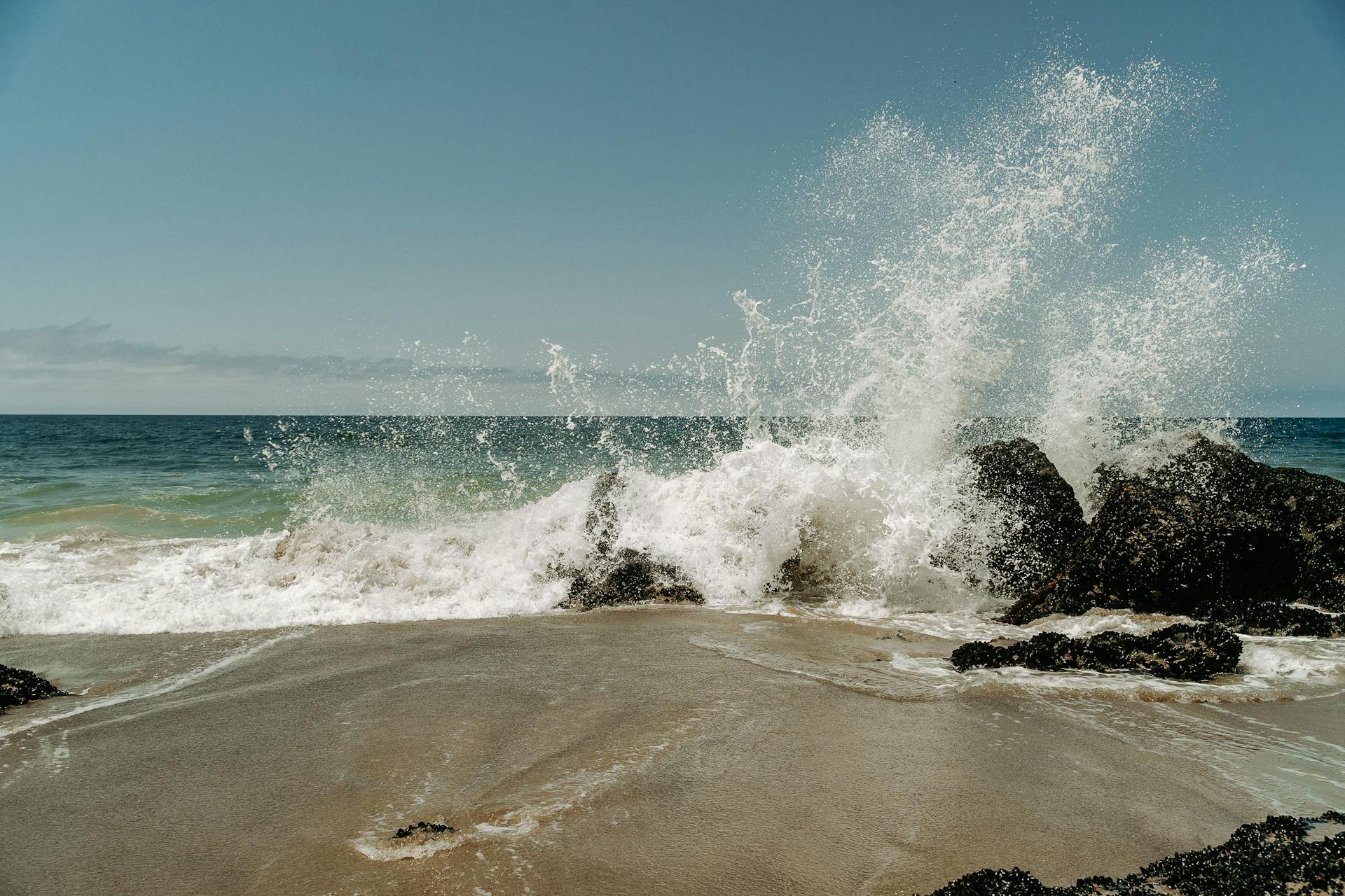 Captivating view of powerful ocean waves crashing against a rocky coastline under a clear blue sky.