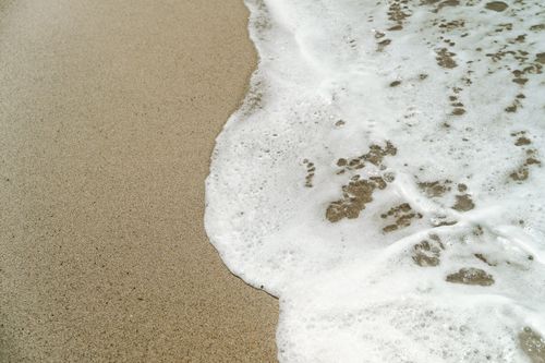 Free Close-up view of ocean waves gently meeting sandy beach with white foam. Stock Photo