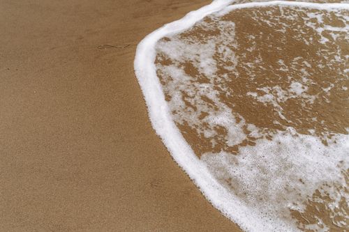 Free Close-up of a sandy beach with gentle waves and foam creating soothing patterns. Stock Photo
