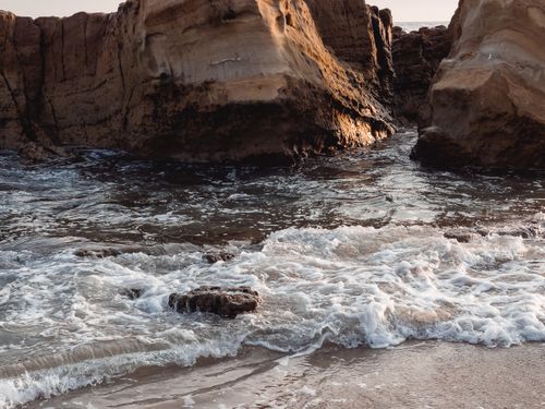 Free Dynamic scene of waves hitting rocky cliffs on a serene beach shore. Stock Photo