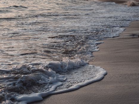 Peaceful beachscape with gentle waves and sandy shoreline at sunset, perfect for tranquil and natural scenes.