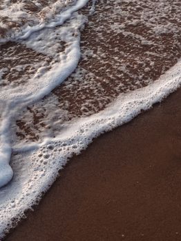 Gentle waves create a soothing pattern on a sandy beach, perfect for nature lovers.