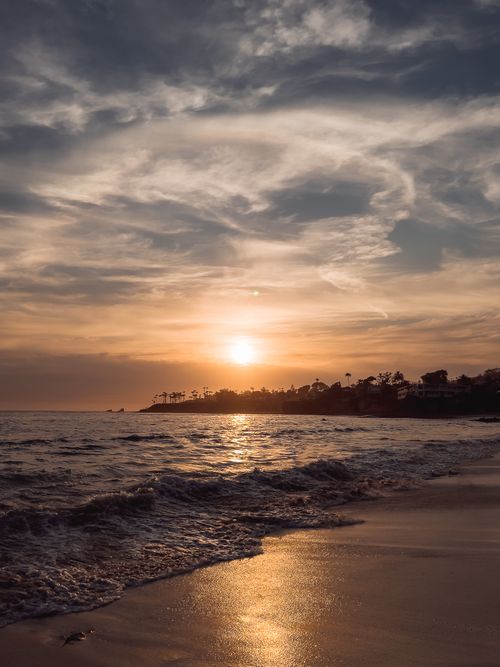 Free A tranquil beach scene with a stunning sunset and dramatic clouds over the sea. Stock Photo