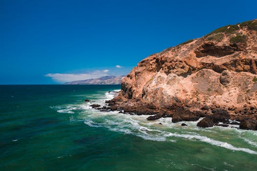A breathtaking view of a rocky coastal cliff and turquoise sea under a clear blue sky.
