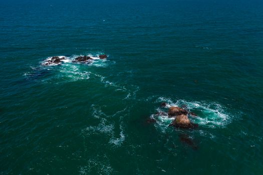 Captivating aerial shot of ocean waves crashing against rocky outcrops in the deep blue sea.