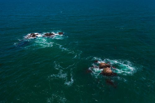 Free Captivating aerial shot of ocean waves crashing against rocky outcrops in the deep blue sea. Stock Photo