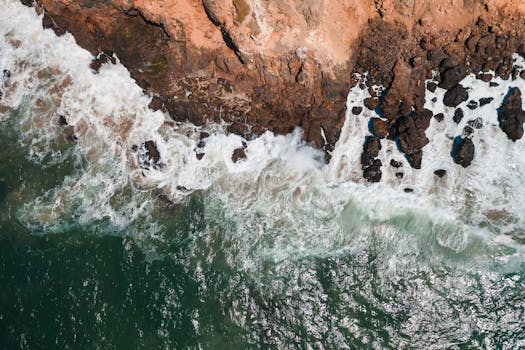 Stunning aerial shot capturing waves crashing against a rocky coastline, showcasing nature's power and beauty.