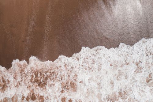 Free Drone shot capturing ocean waves crashing on a sandy shoreline with a unique pattern. Stock Photo